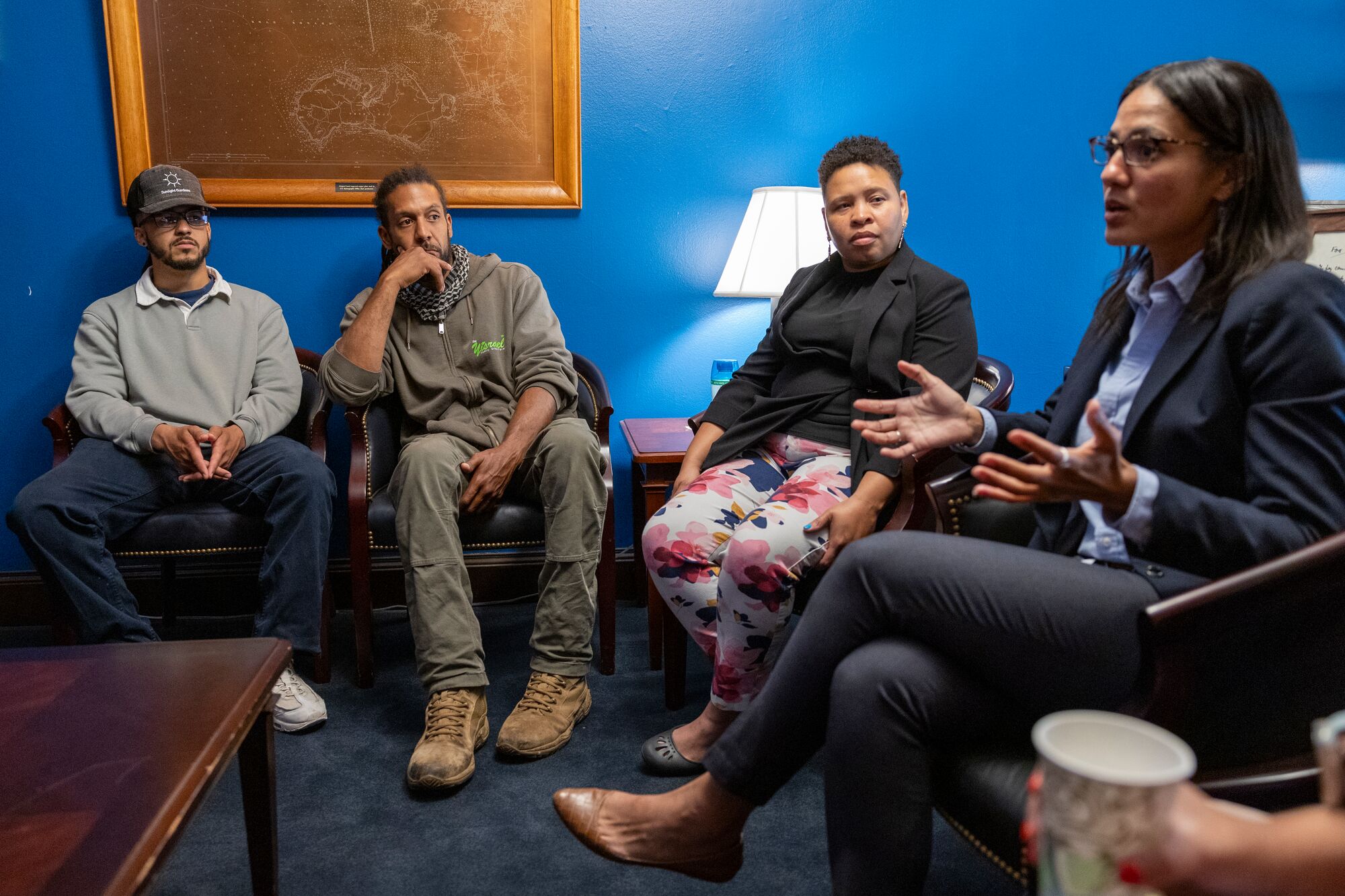 Farm Bill 2024 Lobby Day on Capitol Hill Four people are seated around a small table in an office meeting room with bright blue walls and a vintage map framed on the wall. A person in a dark blue pantsuit is speaking with outstretched hands.
