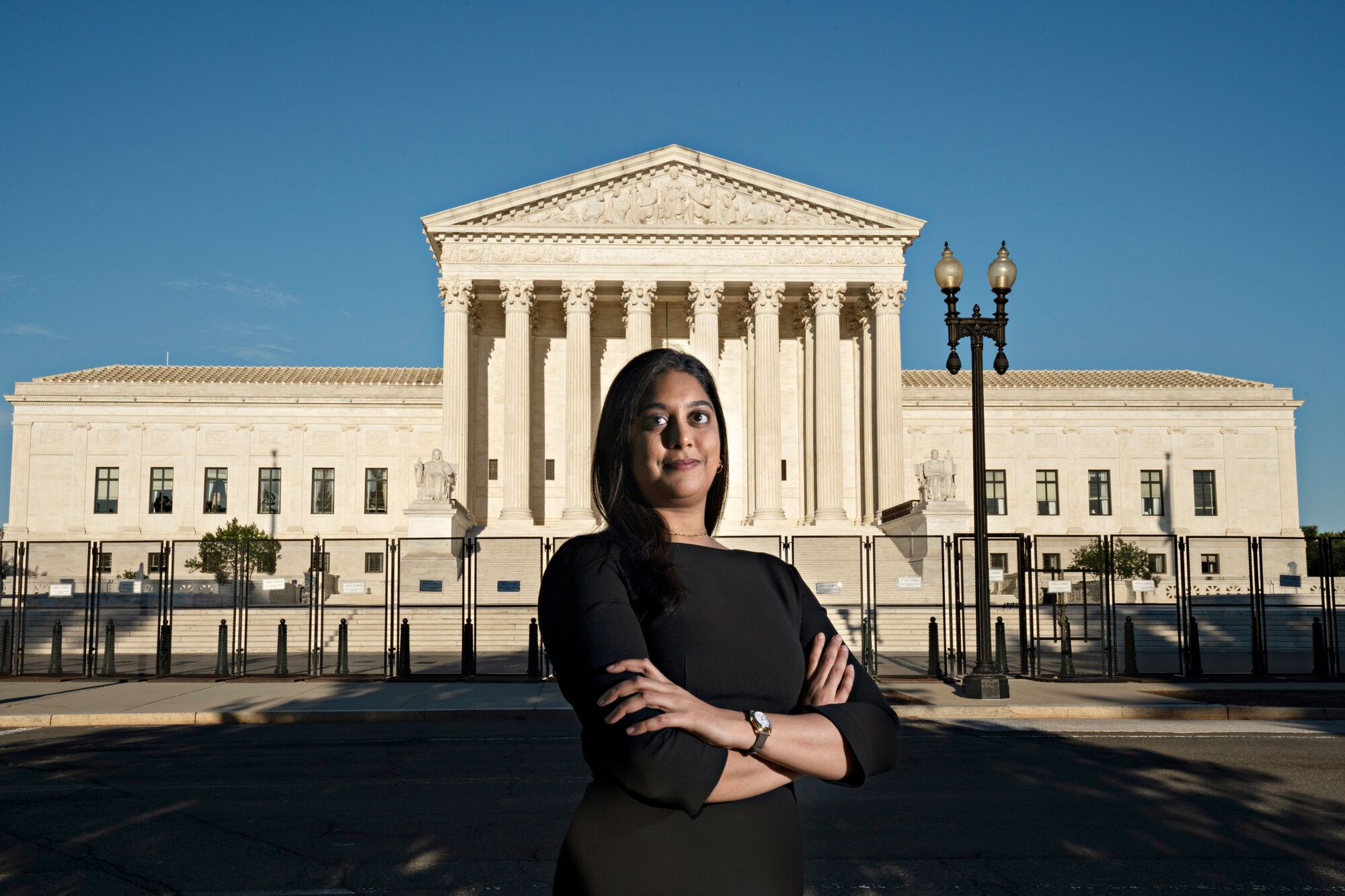 A person dressed in black stands confidently with arms folded in front of the U.S. Supreme Court building.