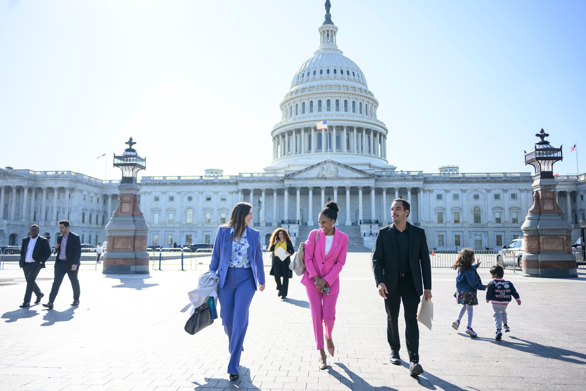 Members of Earthjustice and El Puente cheerfully walk out from the main entrance of the U.S. Capitol building, with the U.S. flag flying in front of the building's classic rotunda, on a bright sunny day, with children and other members of the public in the plaza.