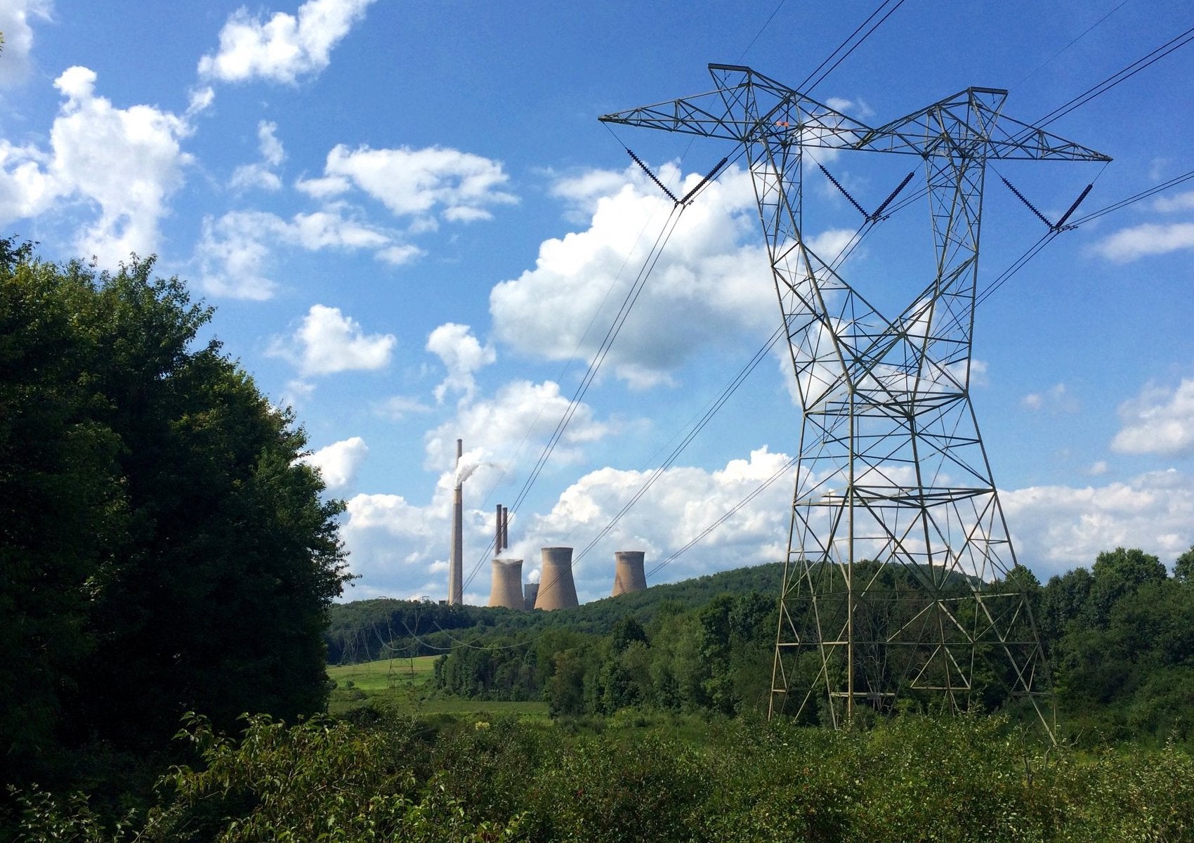 High-tension power lines in the foreground with a power plant in the background.