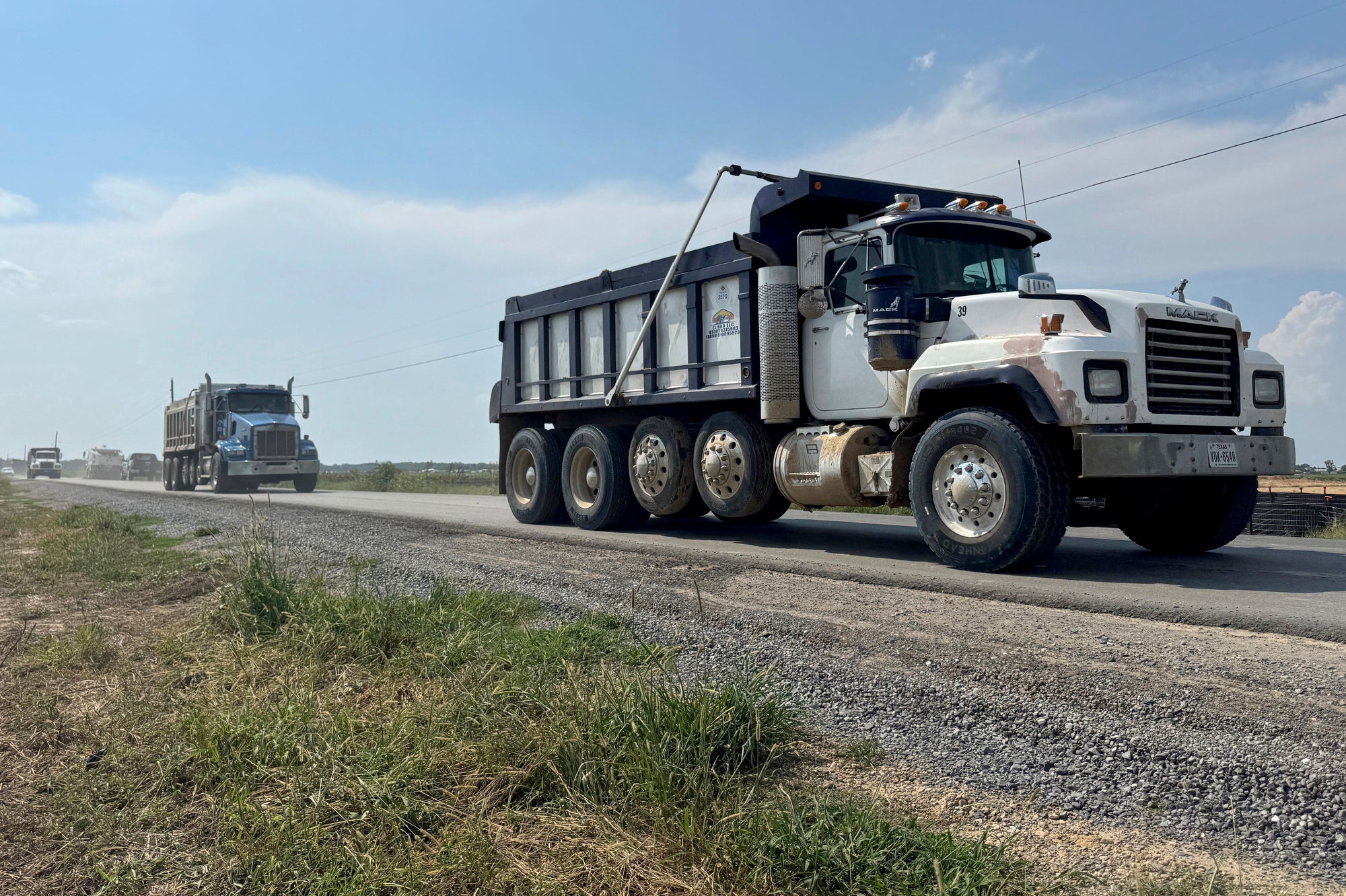 Large dump trucks drive down a rural road.