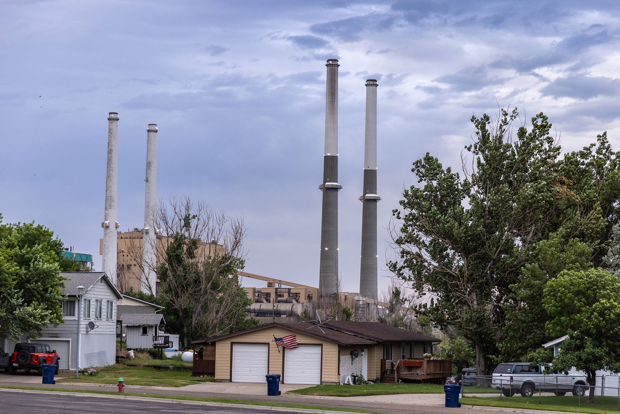 Two sets of tall double smokestacks loom over residential homes. Large portions of the Colstrip power plant are clearly visible directly behind the hoems.