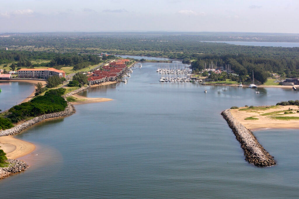 An aerial view of a bay with a resort and marina in the middle distance. Beyond that is a forest and more water.