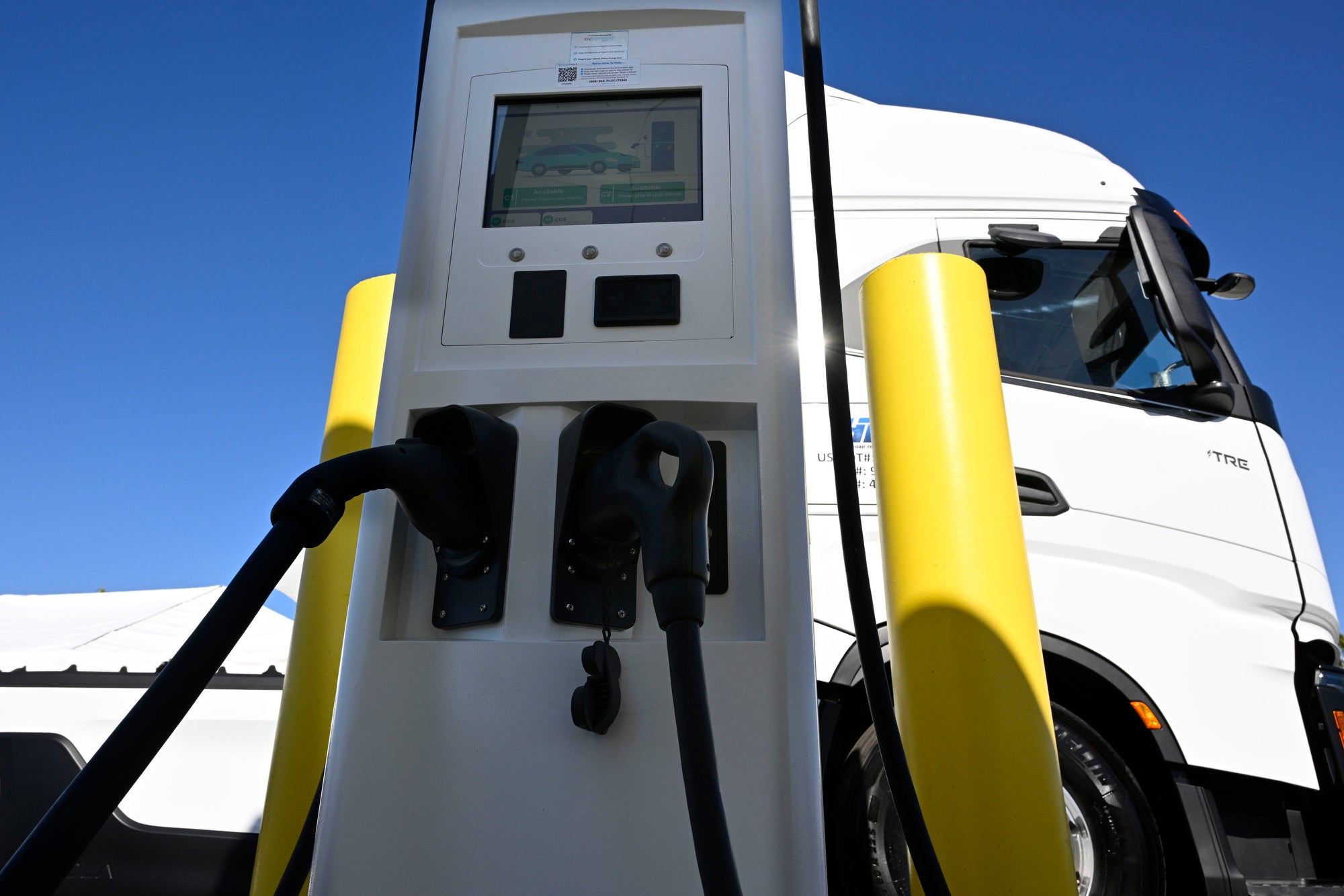 A white semi truck next to a charging station, the photo is close at a low angle.