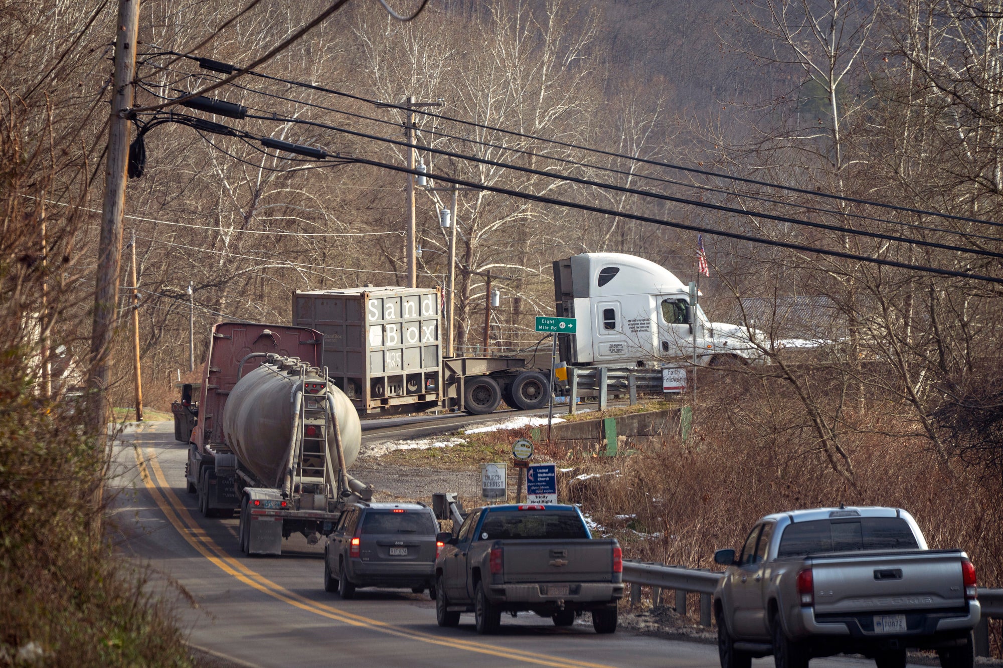 Semi trucks turn up a rural road with cars following them
