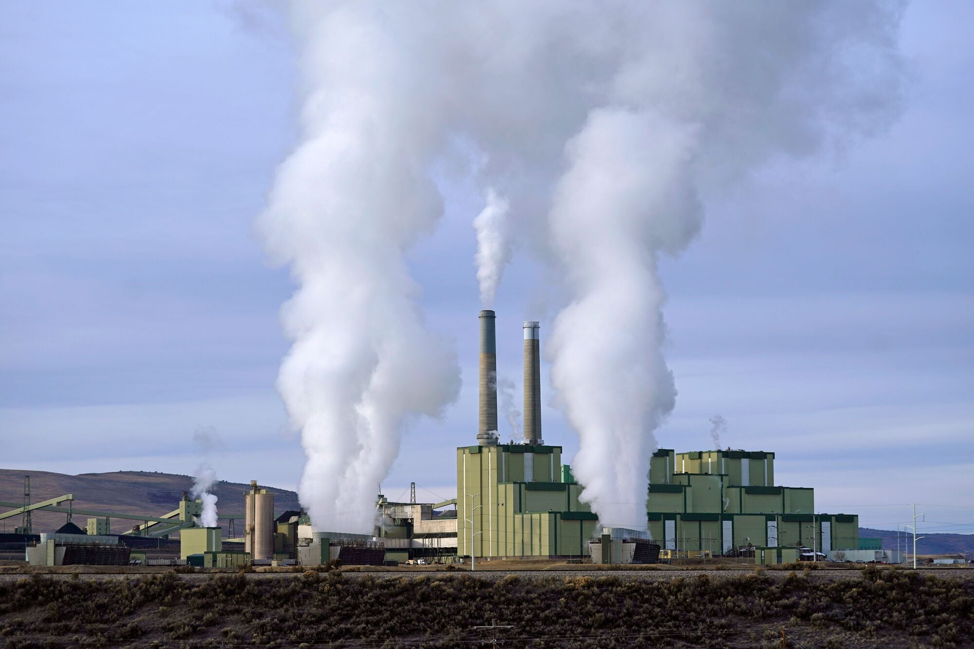 The Craig Station coal plant is dwarfed by large plumes of white steam that bloom upwards into the partly overcast sky.
