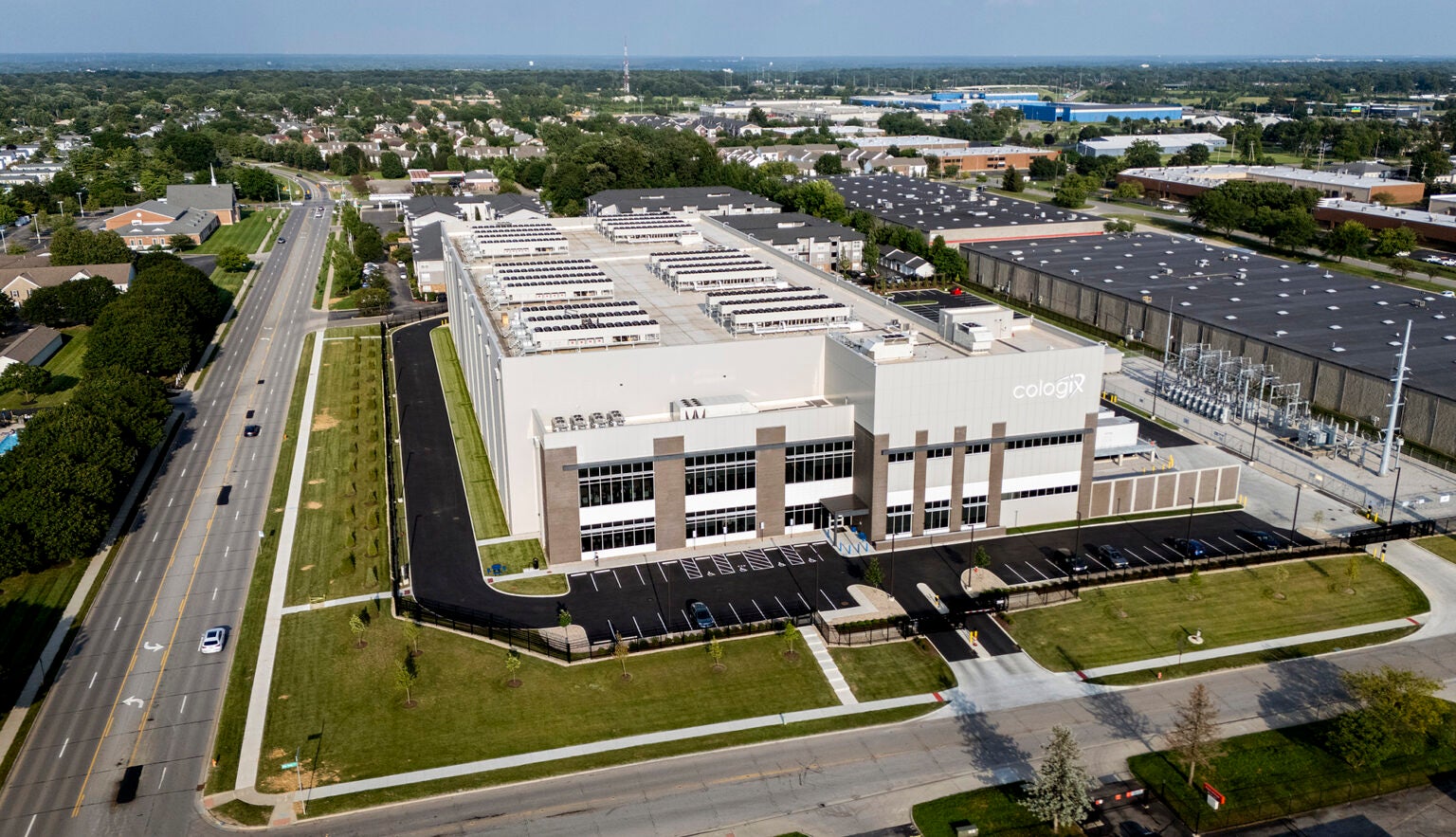 A large industrial building sits on the corner of tree-lined city streets, surrounded by homes, apartment buildings and a church.
