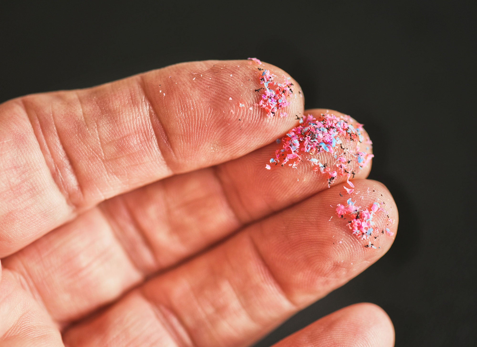 A bare hand shows countless tiny fragments of colorful plastics stuck to the fingertips.