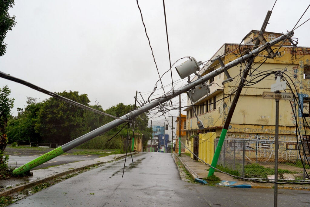 The view of an empty street of a town or city with a utility pole falling across the street, close to touching the ground.