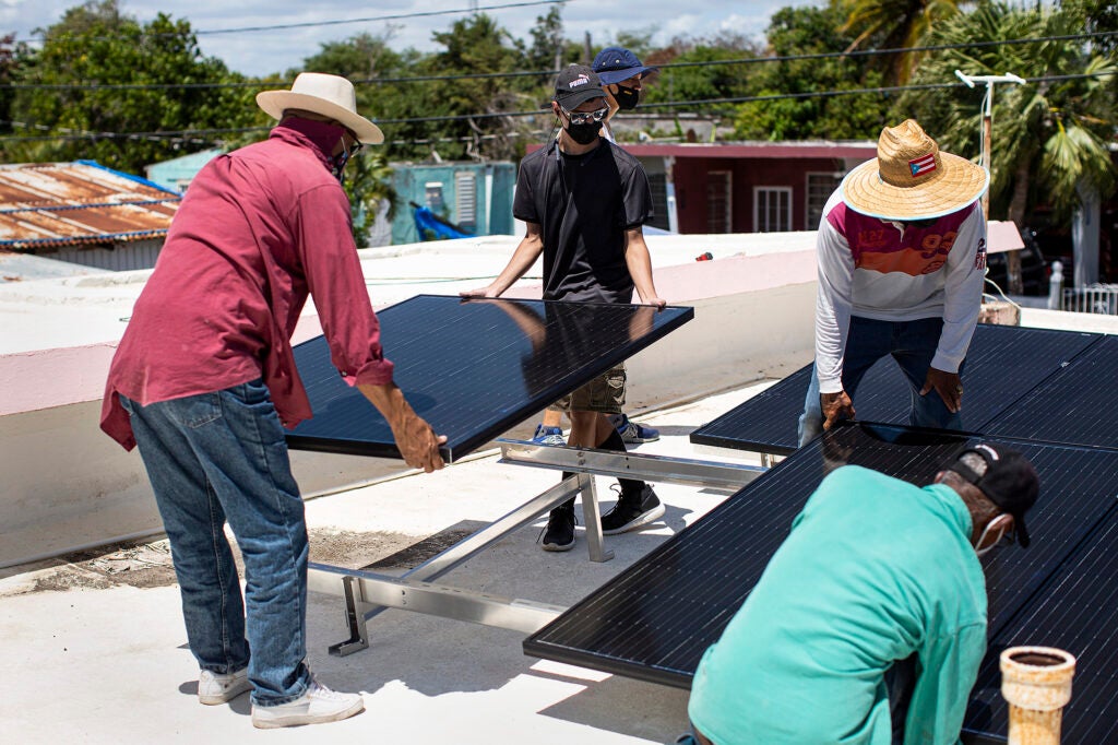 People install solar panels on a flat, white rooftop.