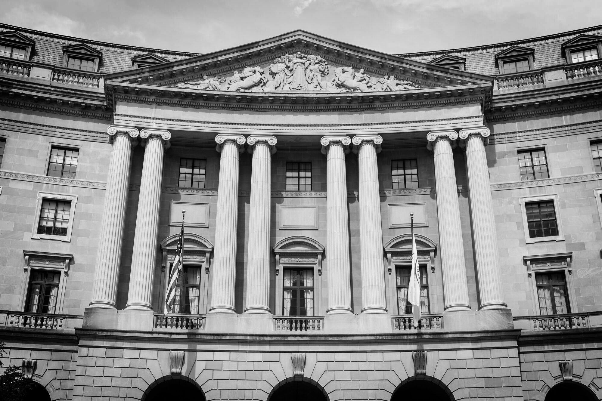 A black-and-white photo of the front of the William Jefferson Clinton Federal Building, home to the U.S. Environmental Protection Agency. The grand, curved stone facade has four sets of double pillars that stretch up three floors high.