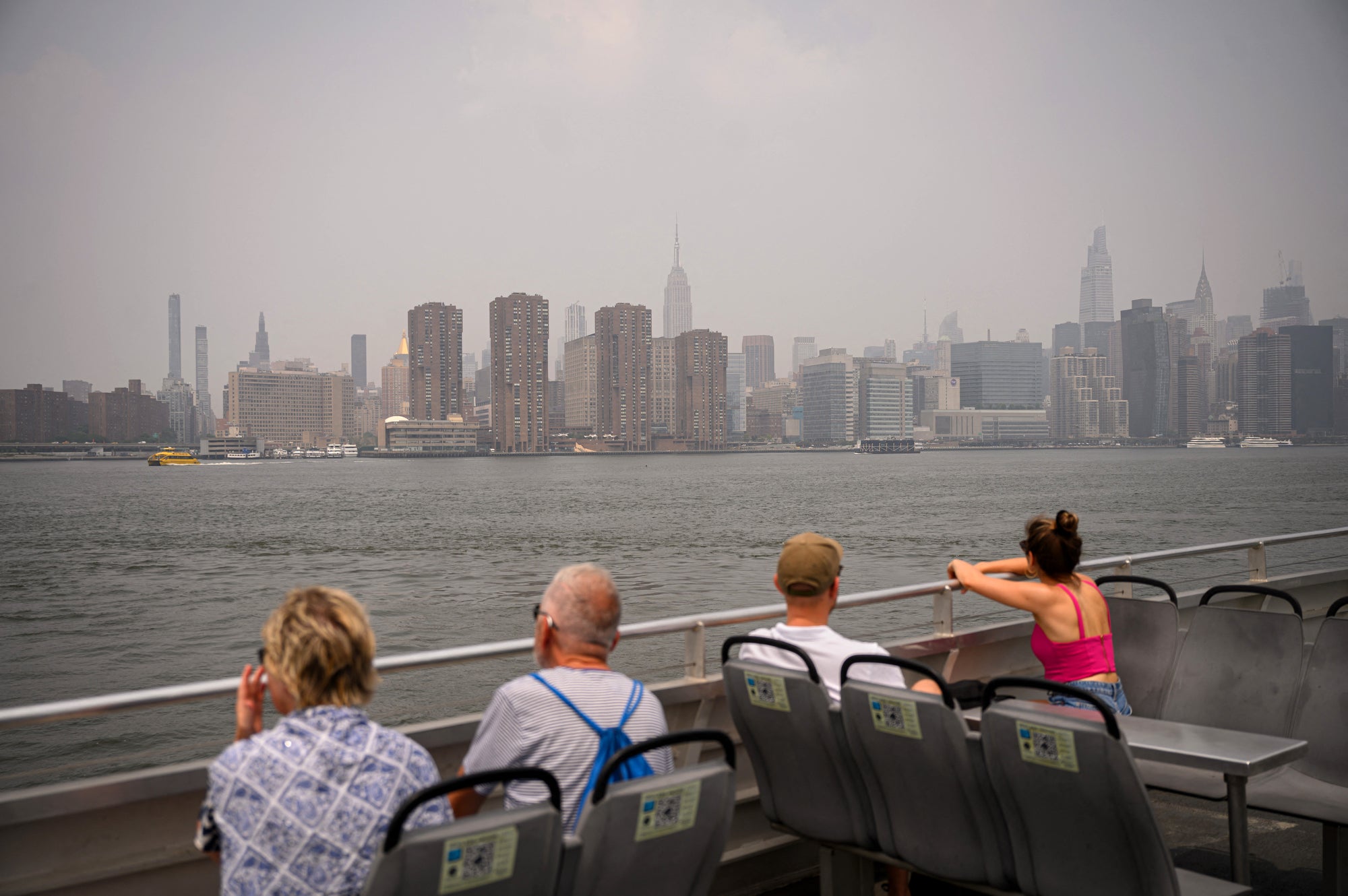 Four people on a ferry look across the water at a very smoky New York skyline.
