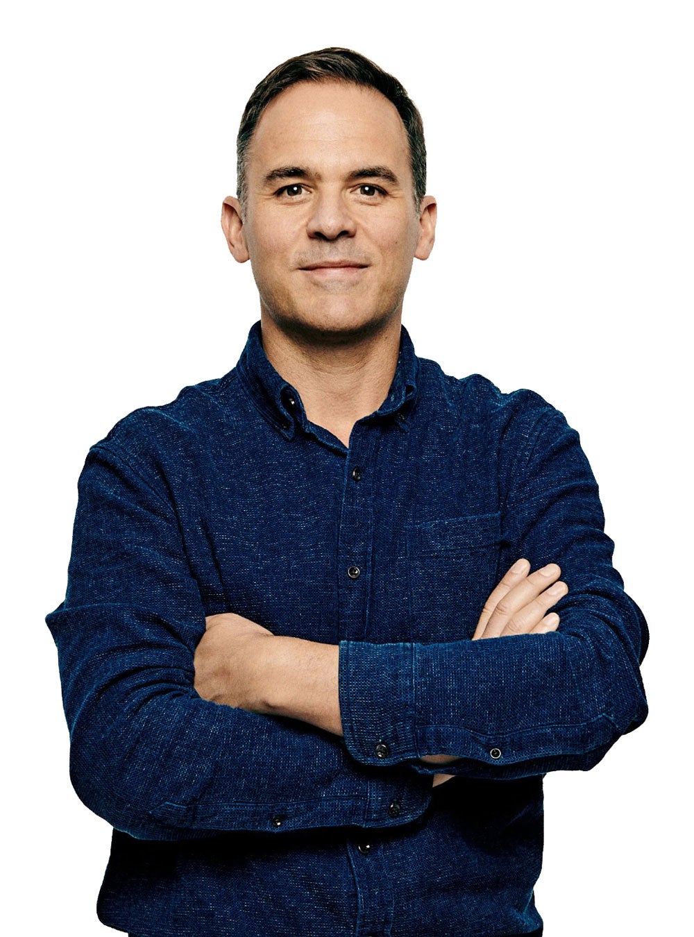 David Gelles stands facing the viewer with a slight smile, wearing a dark blue collared shirt, with his arms folded across his chest.