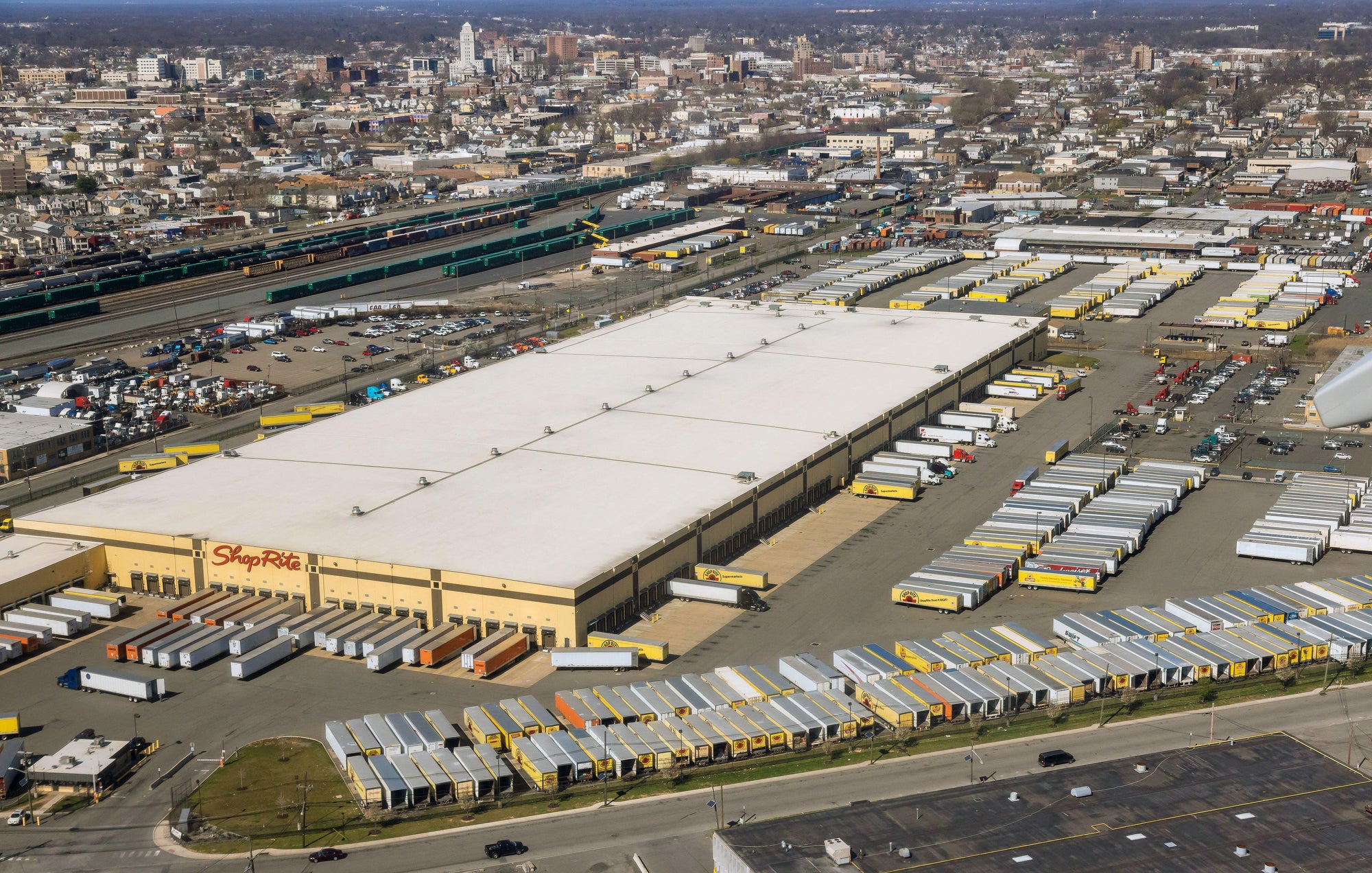 An aerial photo of a large warehouse surrounded by semi trailers, then homes in the near distance.