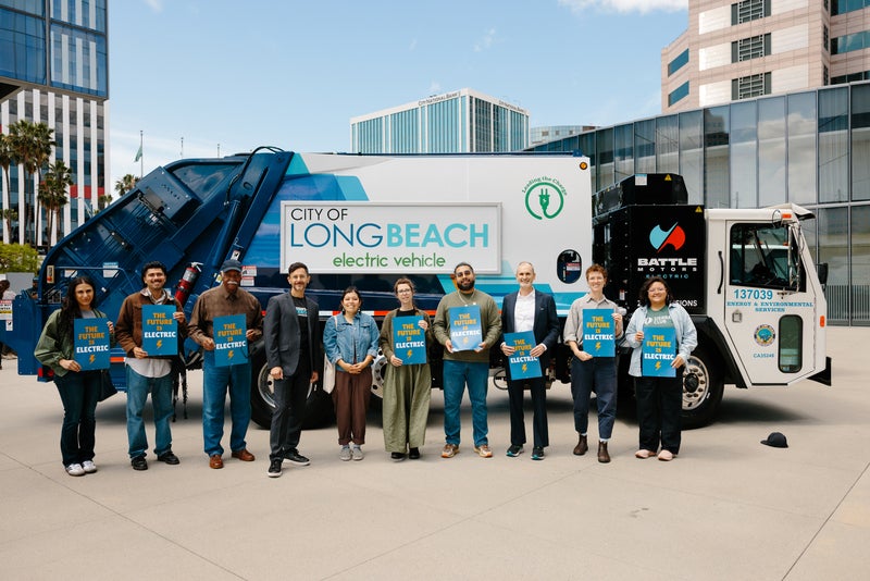 Coalition of advocates holding signs stand in front of electric garbage truck