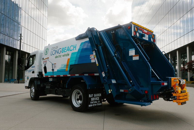 Electric garbage truck parked next to two buildings in Long Beach