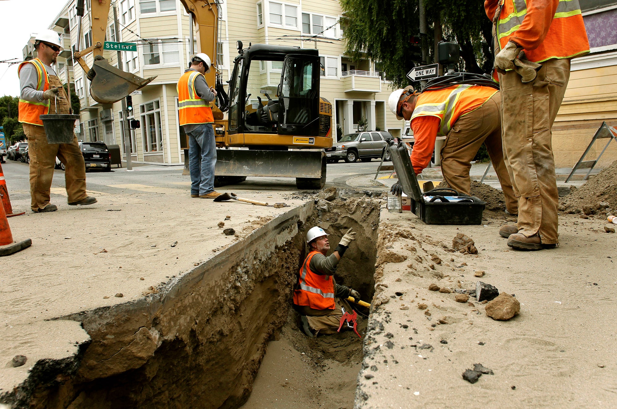 A group of men work in and around a ditch cut into a residential street in San Francisco.