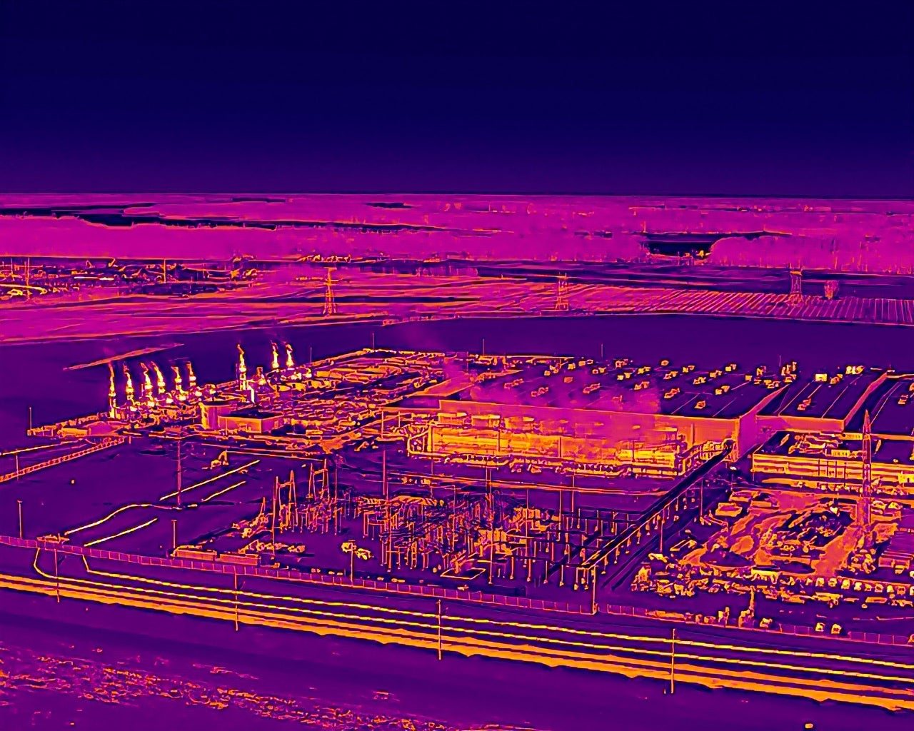 A purple-hued thermal image shows emissions from a row of turbines as bright yellow. The emissions are not visible with the unaided human eye.