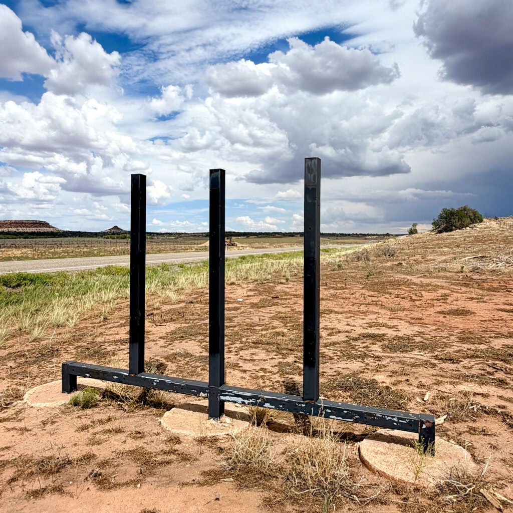 Blue sky and an expansive landscape is visible through an empty metal scaffolding frame that used to hold a large sign.
