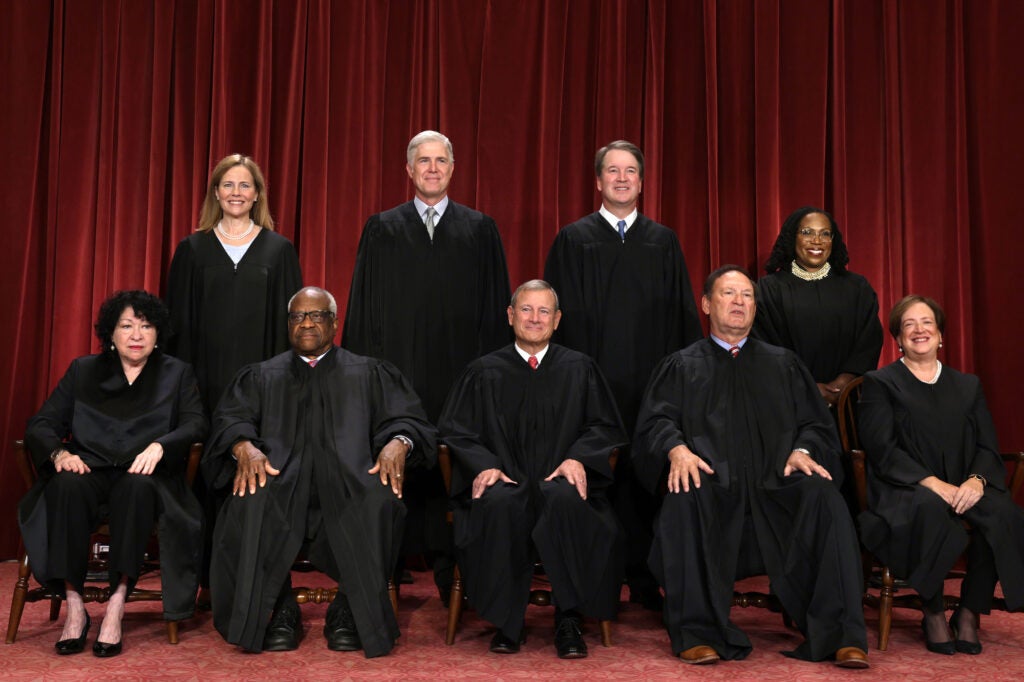 Nine supreme court justices in black robes in two rows in front of a red curtain background.