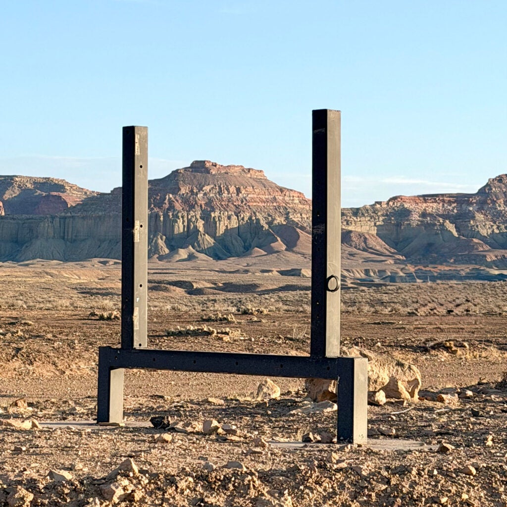 Blue sky and an expansive landscape is visible through an empty metal scaffolding frame that used to hold a large sign.