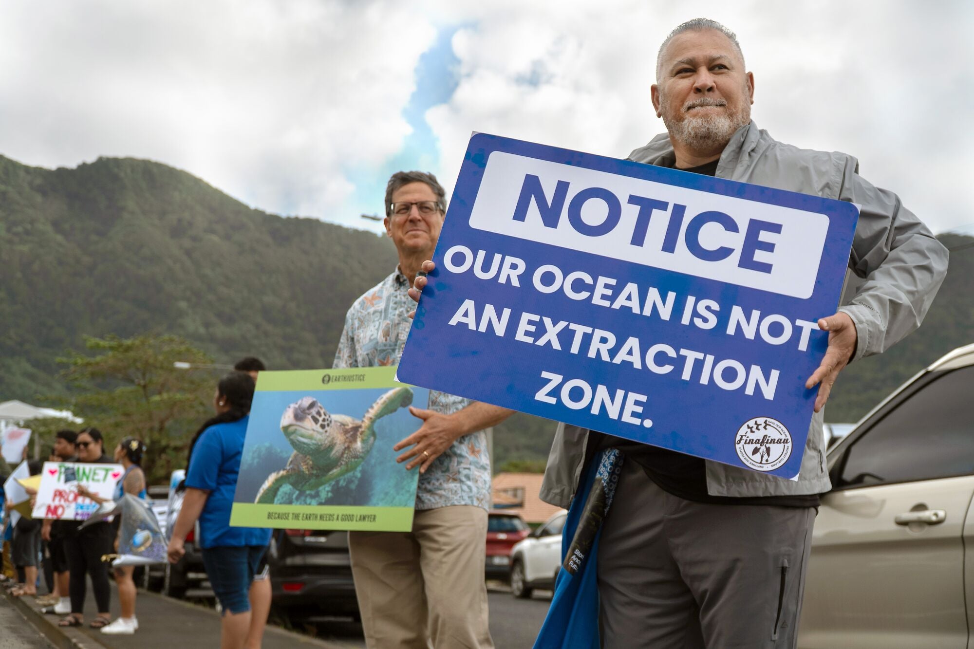 Earthjustice attorney David Henkin stands, left, with Rudy Bartley, right, a member of the nonprofit groups Faʻasao Amerika Samoa and Puipui Measina a Amerika Samoa. They take part in the Stand with the Moana demonstration to support and protect the ocean on July 16, 2026 on the Utulei shore in American Samoa. Rudy holds a sign that says "Notice: Our Ocean Is Not An Extraction Zone."