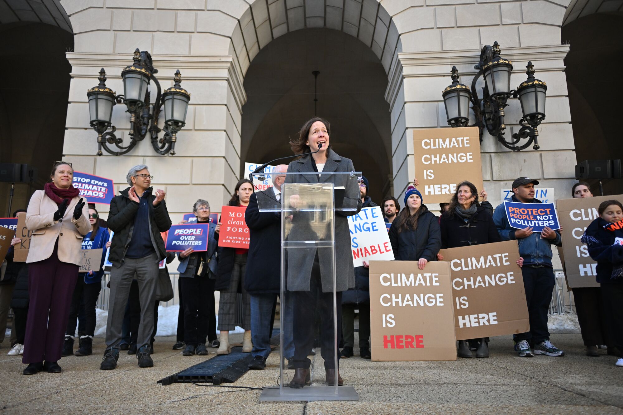 Attendees outside the Environmental Protection Agency Building during a press conference. Many are holding signs that say "climate change is here," "protect people, not polluters," "people over polluters," and more. Standing at the podium is Earthjustice Vice President of Litigation for Climate and Energy Jill Tauber.
