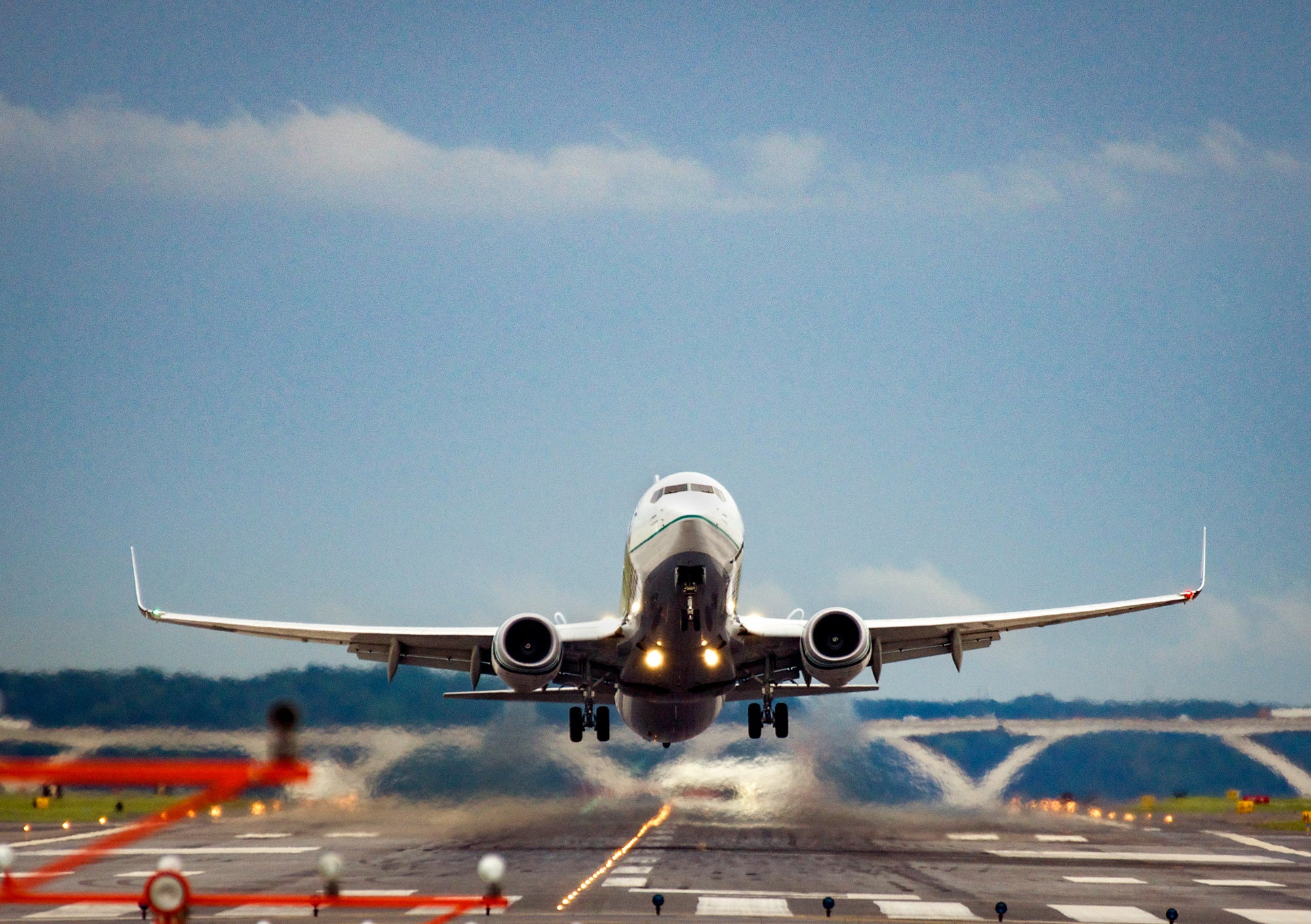 A plane flies towards the camera as it lifts off from the runway at a large airport.