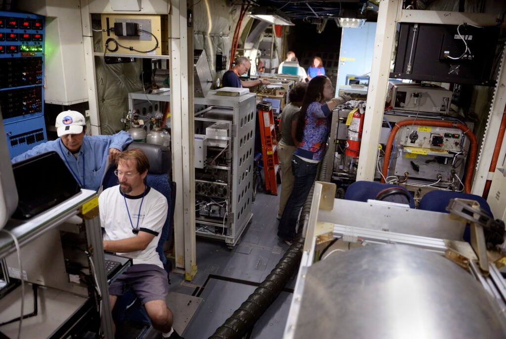 About eight people work in different stations in a large airplane filled with scientific equipment.