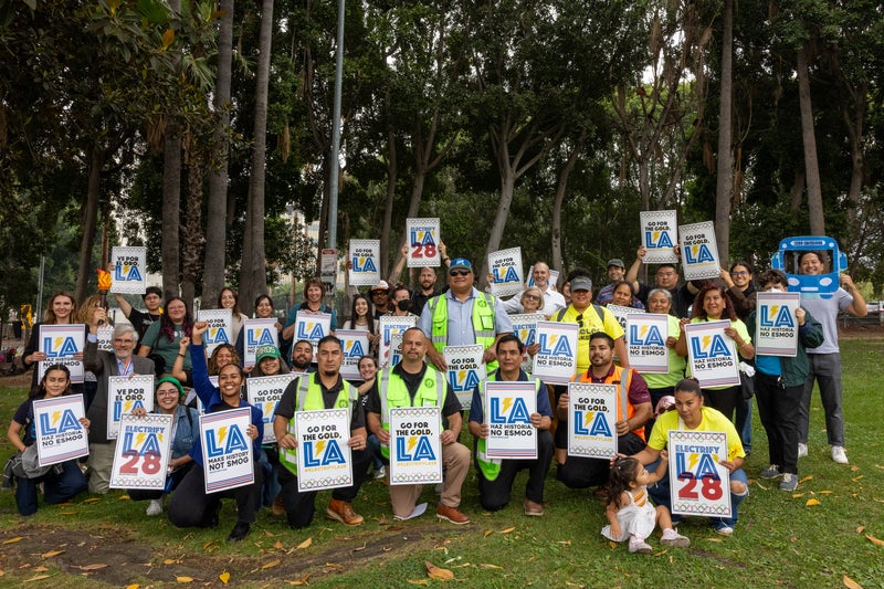 Group of coalition advocates hold signs about electrifying LA Metro