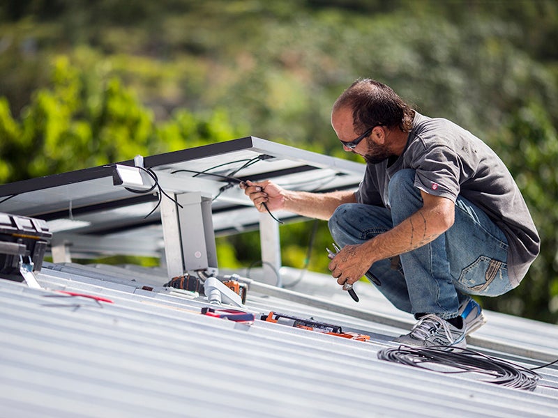 Un técnico instala un sistema de energía solar en una casa en Adjuntas, Puerto Rico, en julio de 2018. La isla forma parte de una lista creciente de estados y ciudades de EE.UU. que se han comprometido con la energía limpia al 100 por ciento.