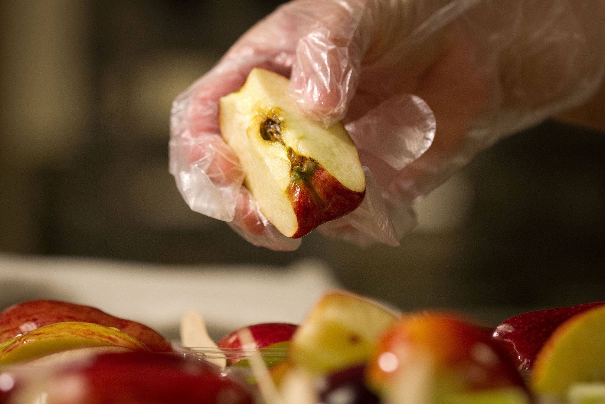 A gloved hand holds up a slice of a red skinned apple.