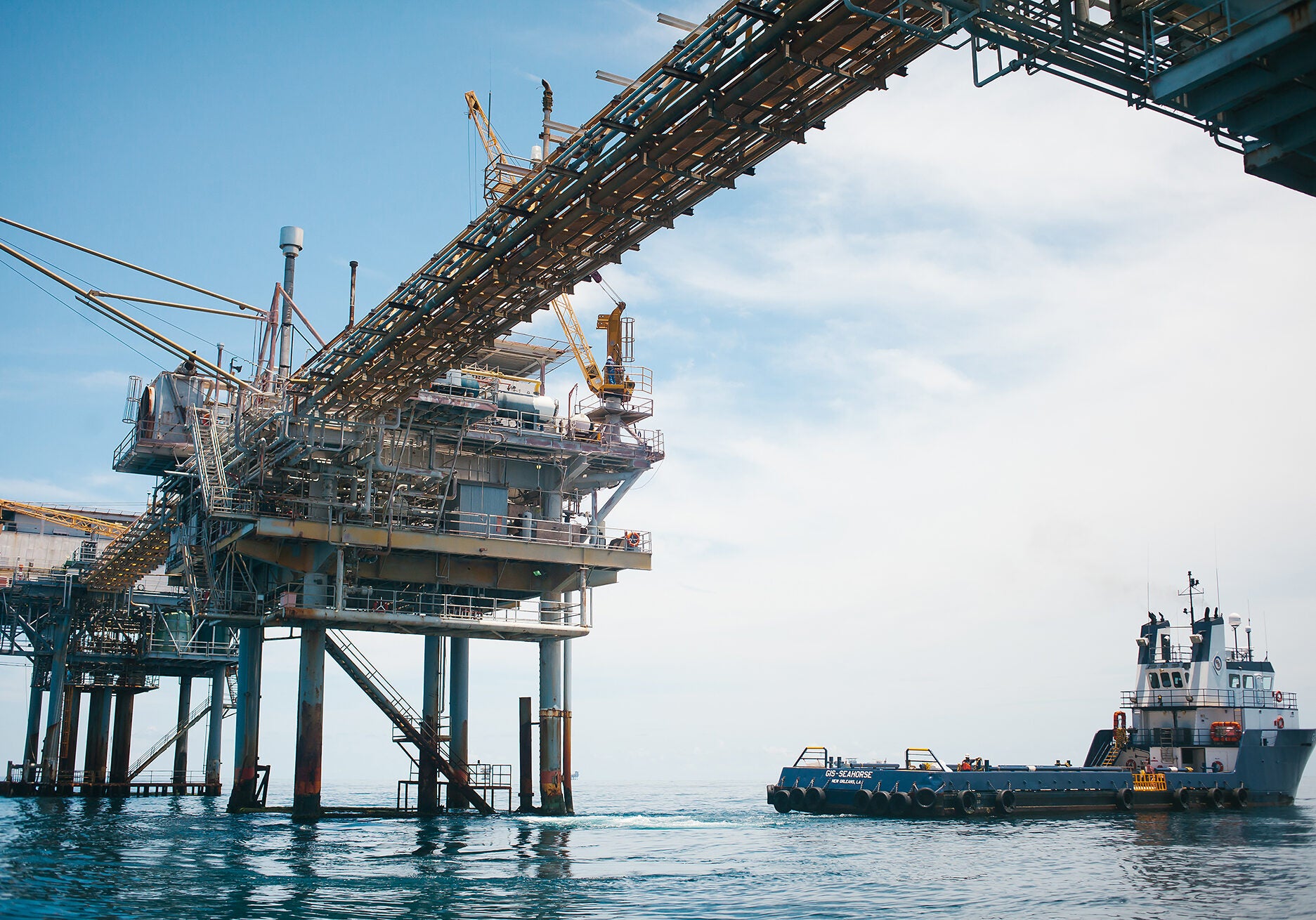 A photo just below an oil and gas rig in the ocean with a boat pulling away.