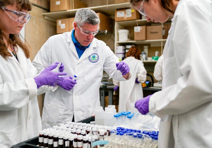 People in lab coats and safety glasses work with samples of material in vials.