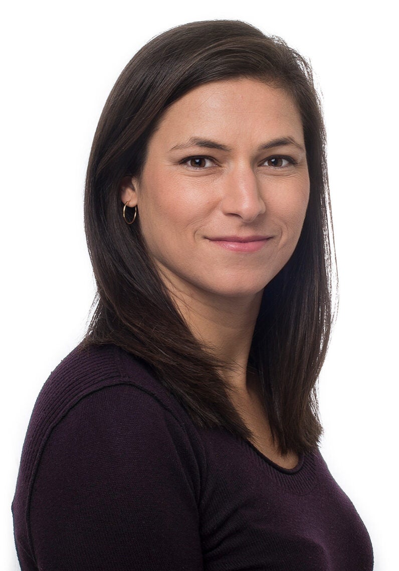 Anna looks directly at the viewer with a friendly, slight smile. She's wearing a dark burgundy top, and stands angled to the viewer's right, in front of a white backdrop.