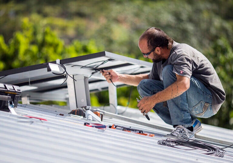 Un técnico instala un sistema de energía solar en una casa en Adjuntas, Puerto Rico, en julio de 2018. La isla forma parte de una lista creciente de estados y ciudades de EE.UU. que se han comprometido con la energía limpia al 100 por ciento.