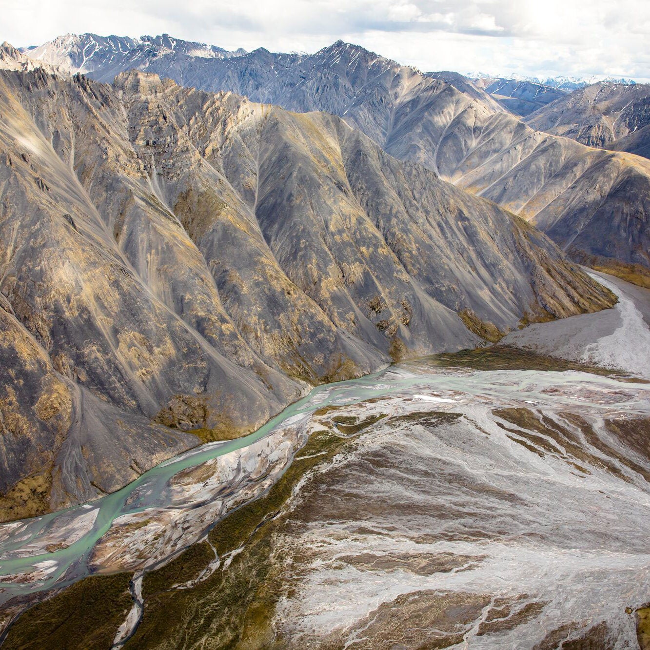 Brown and gray mountain ranges with a river running at the base. The river is green and blue in different areas.