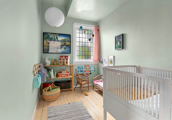 A baby's room with a white crib in the foreground, with toys and decoration and light streaming in from a large window.