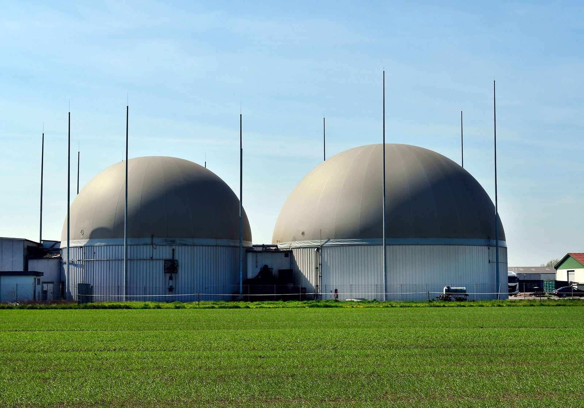 Biogas Production Facilities Two large grey semi-circular buildings rise out of bright green agricultural fields.