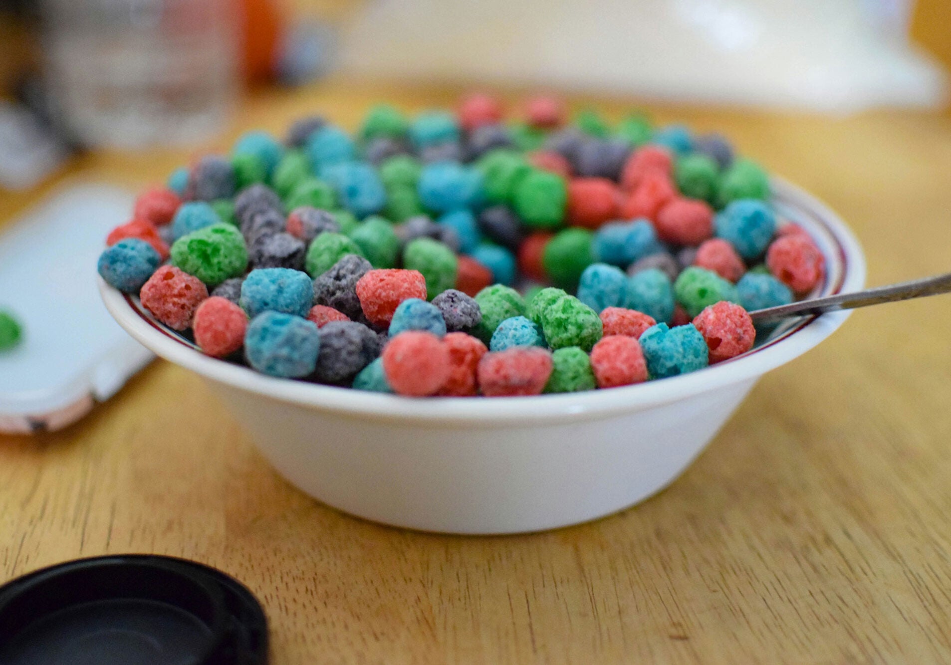 A white bowl of brightly colored cereal on a wooden table.
