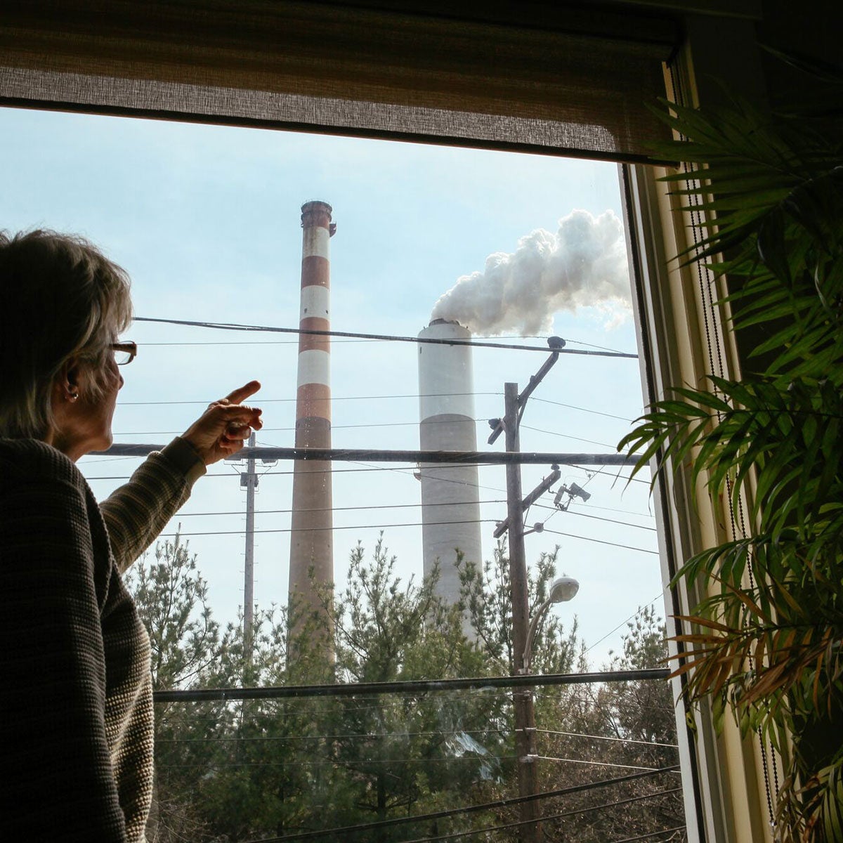 A woman inside her home in Springdale, Penn., in 2010, points out the window at the smokestacks of Cheswick Generating Station, as they emit soot and toxic air pollutants.