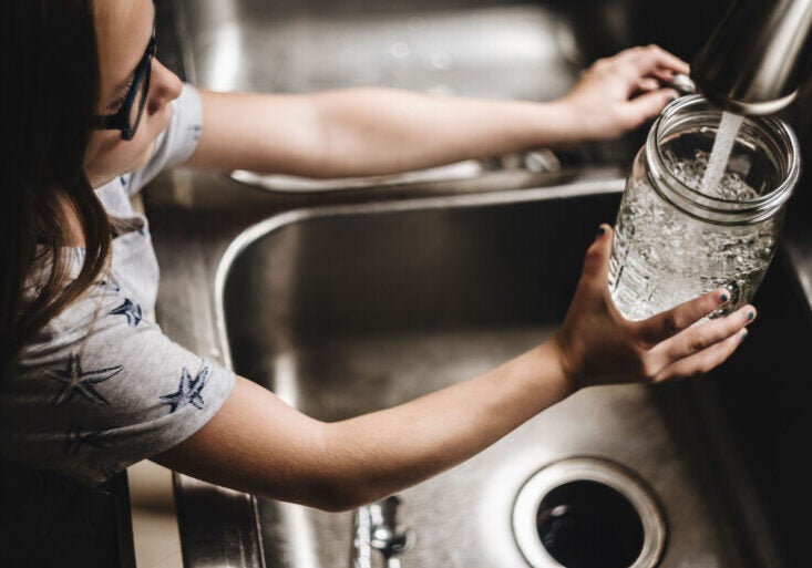 A child fills a drinking glass with water from the faucet.