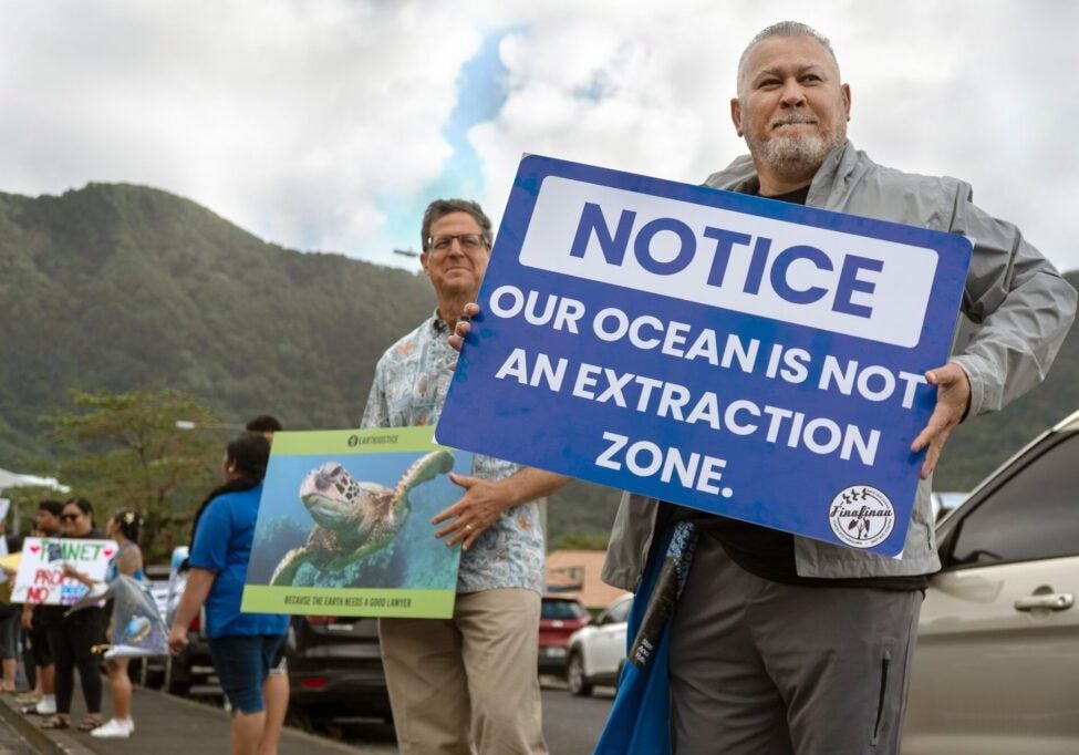 Earthjustice attorney David Henkin stands, left, with Rudy Bartley, right, a member of the nonprofit groups Faʻasao Amerika Samoa and Puipui Measina a Amerika Samoa. They take part in the Stand with the Moana demonstration to support and protect the ocean on July 16, 2026 on the Utulei shore in American Samoa. Rudy holds a sign that says "Notice: Our Ocean Is Not An Extraction Zone."