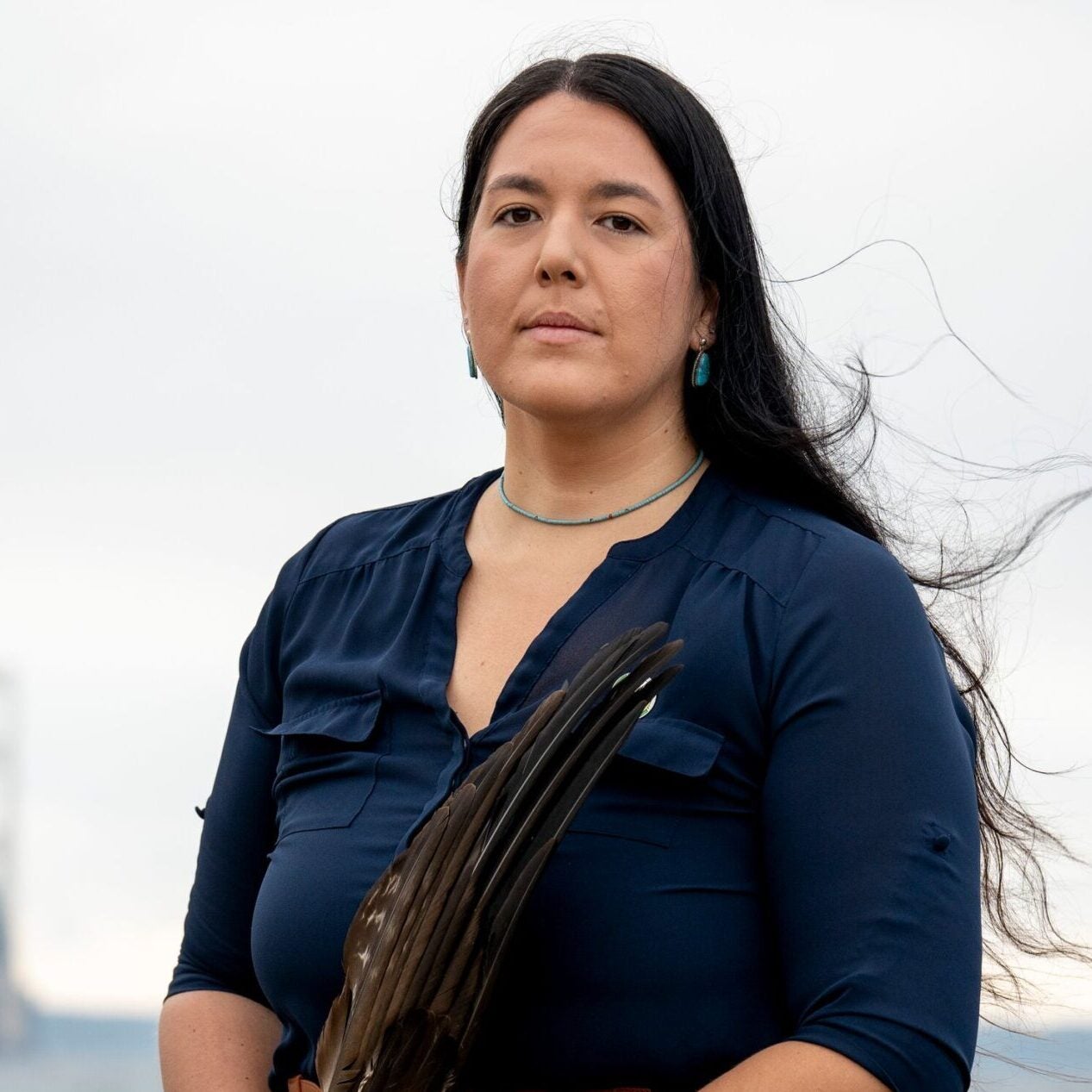 Whitney Gravelle, holding feather in her hand, stands on the bank of the lake.