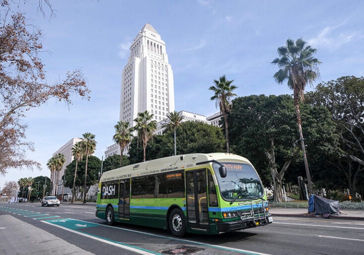 An all electric bus driving on the streets of Los Angeles in front of Los Angeles City Hall.