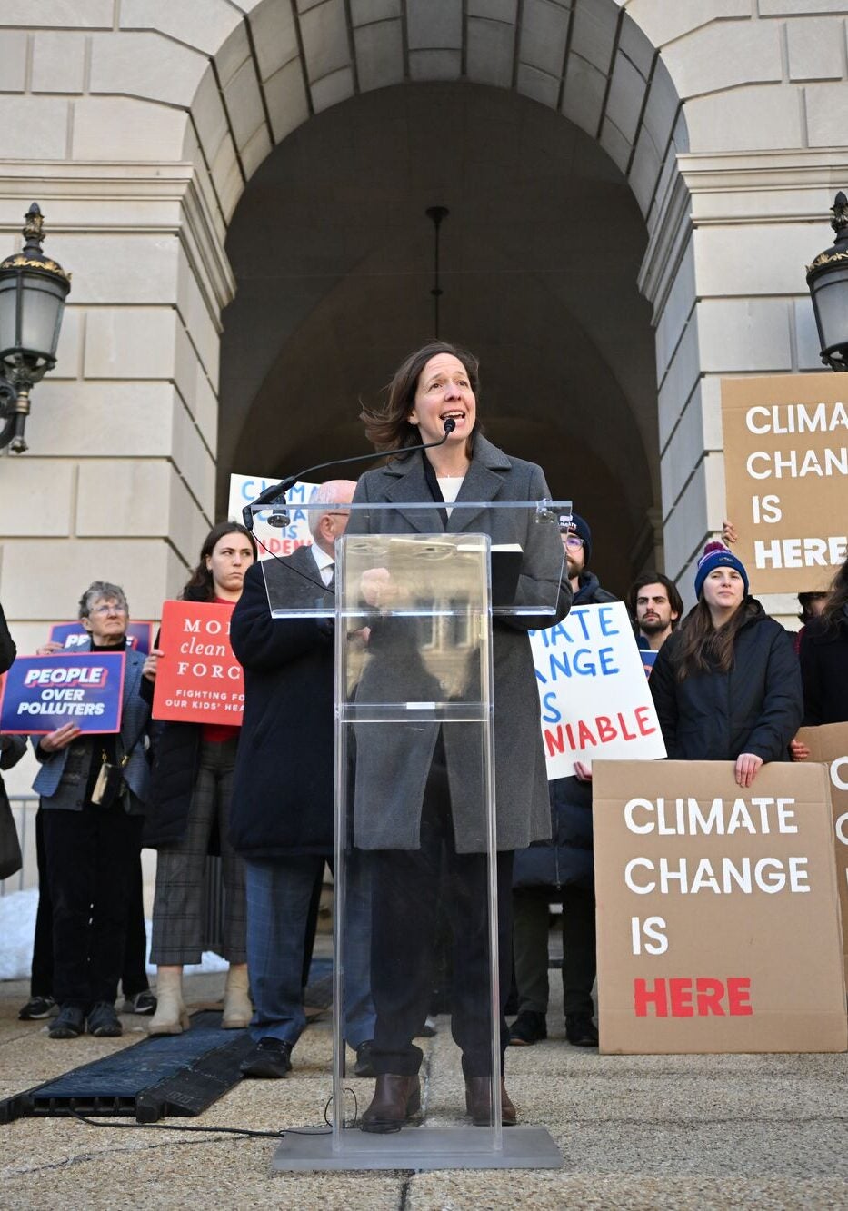 Attendees outside the Environmental Protection Agency Building during a press conference. Many are holding signs that say "climate change is here," "protect people, not polluters," "people over polluters," and more. Standing at the podium is Earthjustice Vice President of Litigation for Climate and Energy Jill Tauber.