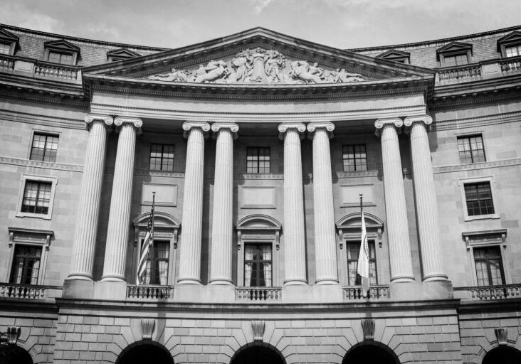 A black-and-white photo of the front of the William Jefferson Clinton Federal Building, home to the U.S. Environmental Protection Agency. The grand, curved stone facade has four sets of double pillars that stretch up three floors high.