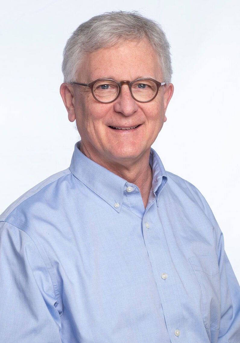Eric looks directly at the viewer with a friendly, open smile. He's wearing glasses and a light blue collared shirt, and standing in front of a white backdrop.