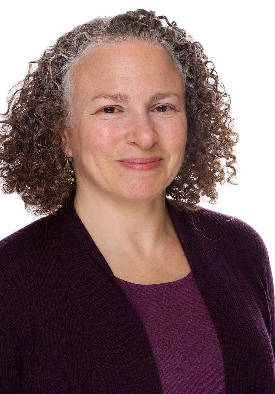 Eve looks directly at the viewer with a friendly smile. She's wearing a dark burgundy knit cardigan and a light burgundy blouse, standing in front of a white backdrop.