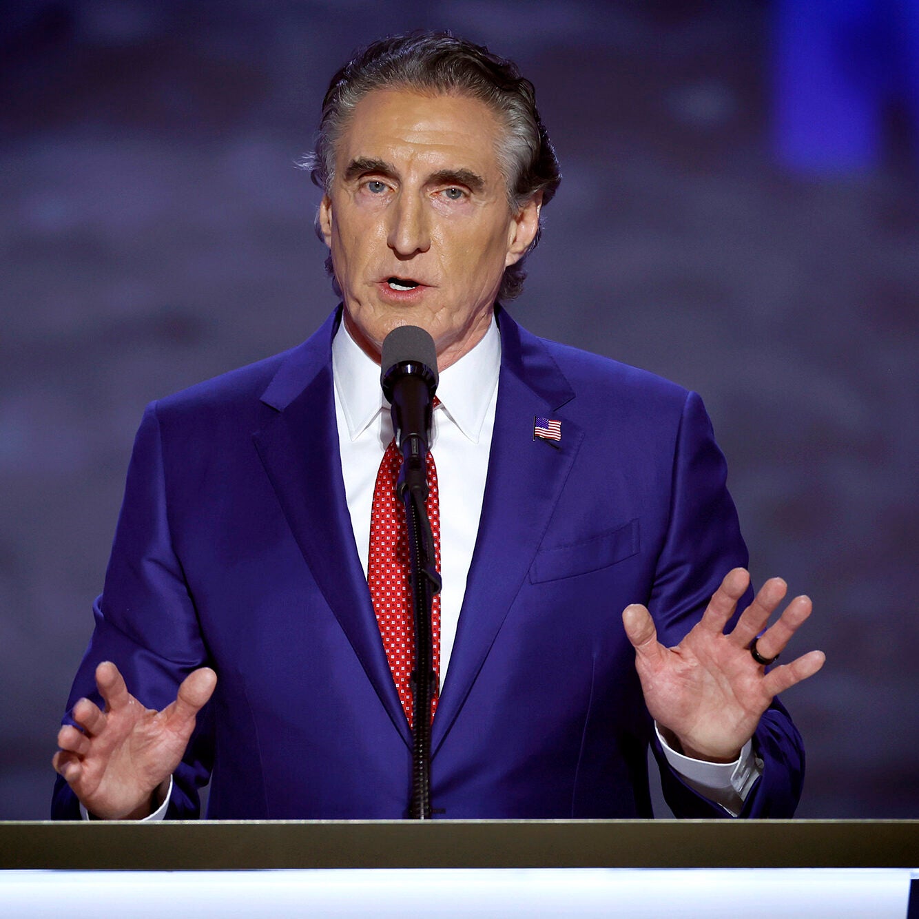 A man in a blue suit speaks at a podium